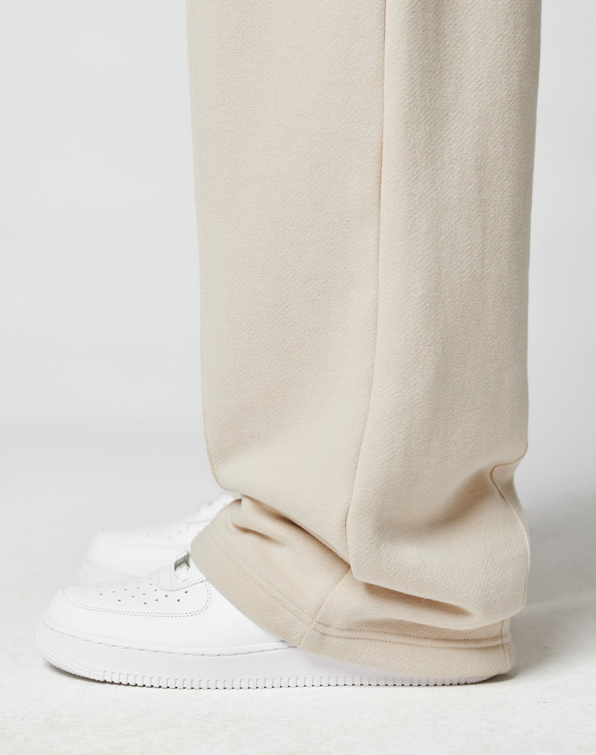 A close-up shows a person wearing LIVE FAST DIE YOUNGs LFDY Pleated Jogger in wide fit beige, featuring an Elastik-Bund, draped over clean white sneakers against a simple white background.