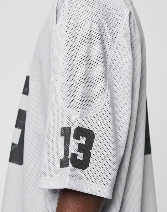 Close-up of a persons arm in the LFDY Mesh Jersey by LIVE FAST DIE YOUNG, featuring black number 13 on the sleeve. The oversize white polyester mesh design offers comfort against a plain, light background.