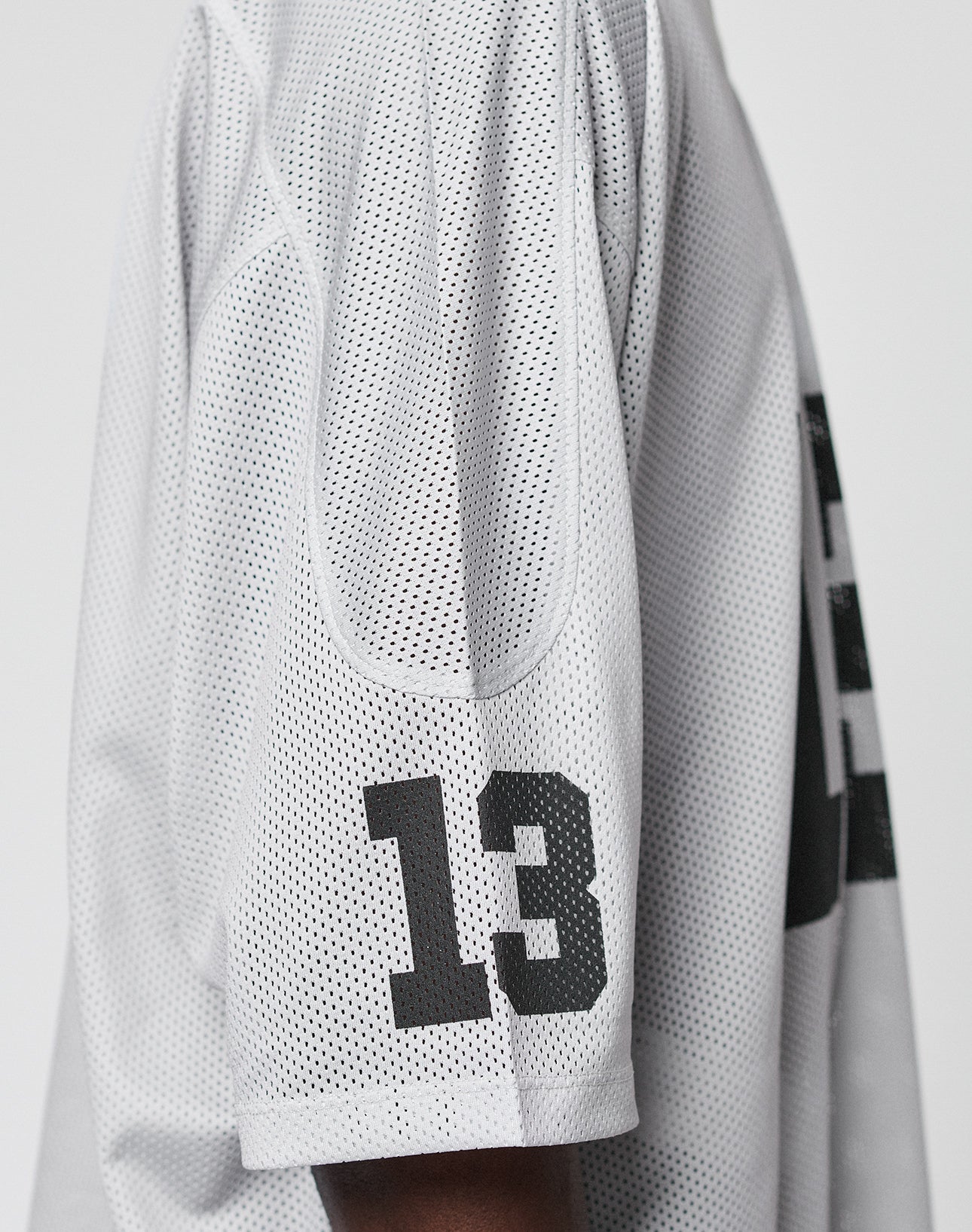 A close-up side view of a person wearing the LFDY Mesh Jersey by LIVE FAST DIE YOUNG, featuring white polyester mesh fabric and bold black number 13 printed on the sleeve.