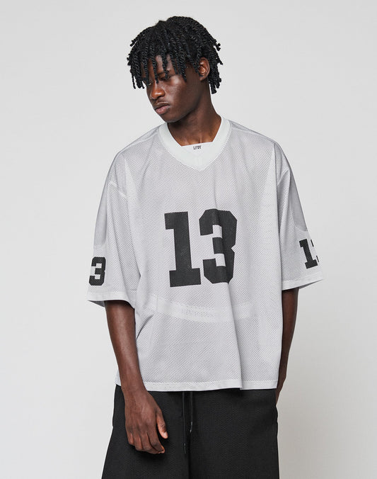 A person with short, textured hair models the oversized LFDY Mesh Jersey by LIVE FAST DIE YOUNG in gray polyester mesh with black number 13 on the front and sleeve, paired with black pants against a plain background.