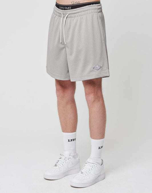 A person wearing LIVE FAST DIE YOUNG Basic Mesh Shorts in light gray with a logo patch, white LIVE FAST boxer waistband, white LFDY socks, and white Nike sneakers stands against a plain white background. | model
