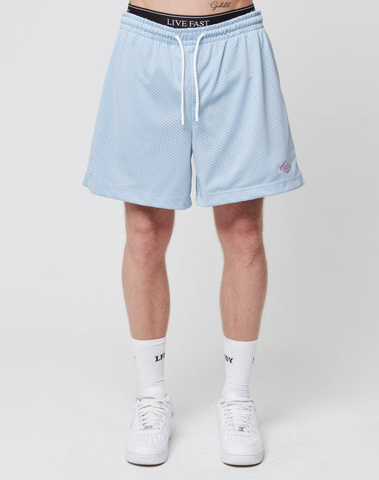 A person stands facing forward in LIVE FAST DIE YOUNG Basic Mesh Shorts with an elastic waistband, white crew socks, and white sneakers. A black waistband with LIVE FAST text is visible above the light blue shorts against a plain white background.