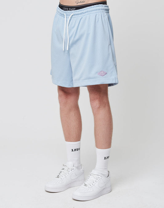 A person stands against a plain background wearing LIVE FAST DIE YOUNG Basic Mesh Shorts in light blue, white crew socks with black text, and white Nike sneakers. Only the lower half of the body is visible. | model