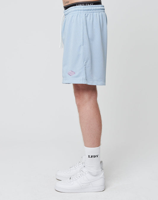 A person stands sideways in LIVE FAST DIE YOUNG Basic Mesh Shorts (light blue), white crew socks with LFDY text, and white Nike sneakers against a plain white background.