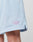 Close-up of a persons upper leg wearing LIVE FAST DIE YOUNG Basic Mesh Shorts in light blue. These regular fit polyester shorts feature an elastic waistband, side slit for comfort, and a small lavender diamond-shaped GIVELAST patch near the hem.