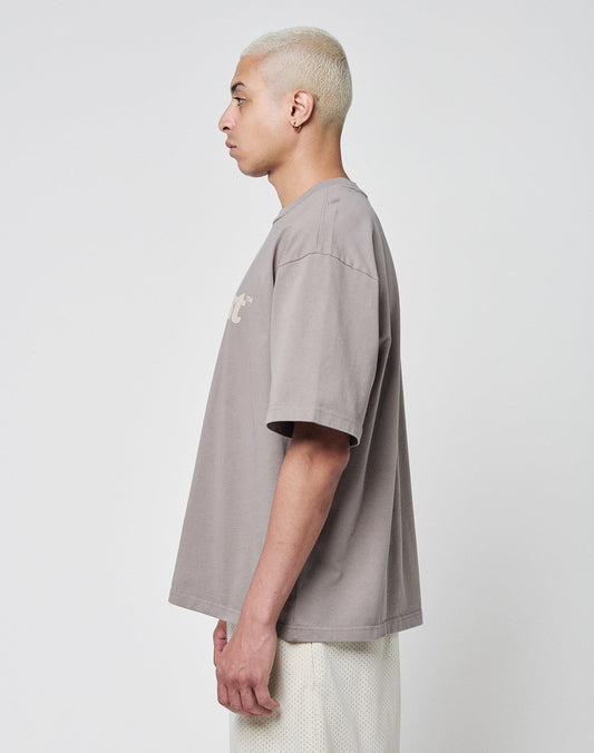 A person with short, bleached blond hair stands in profile against a plain background, wearing the LIVE FAST DIE YOUNG Basic Tee in an oversized fit and white mesh shorts.