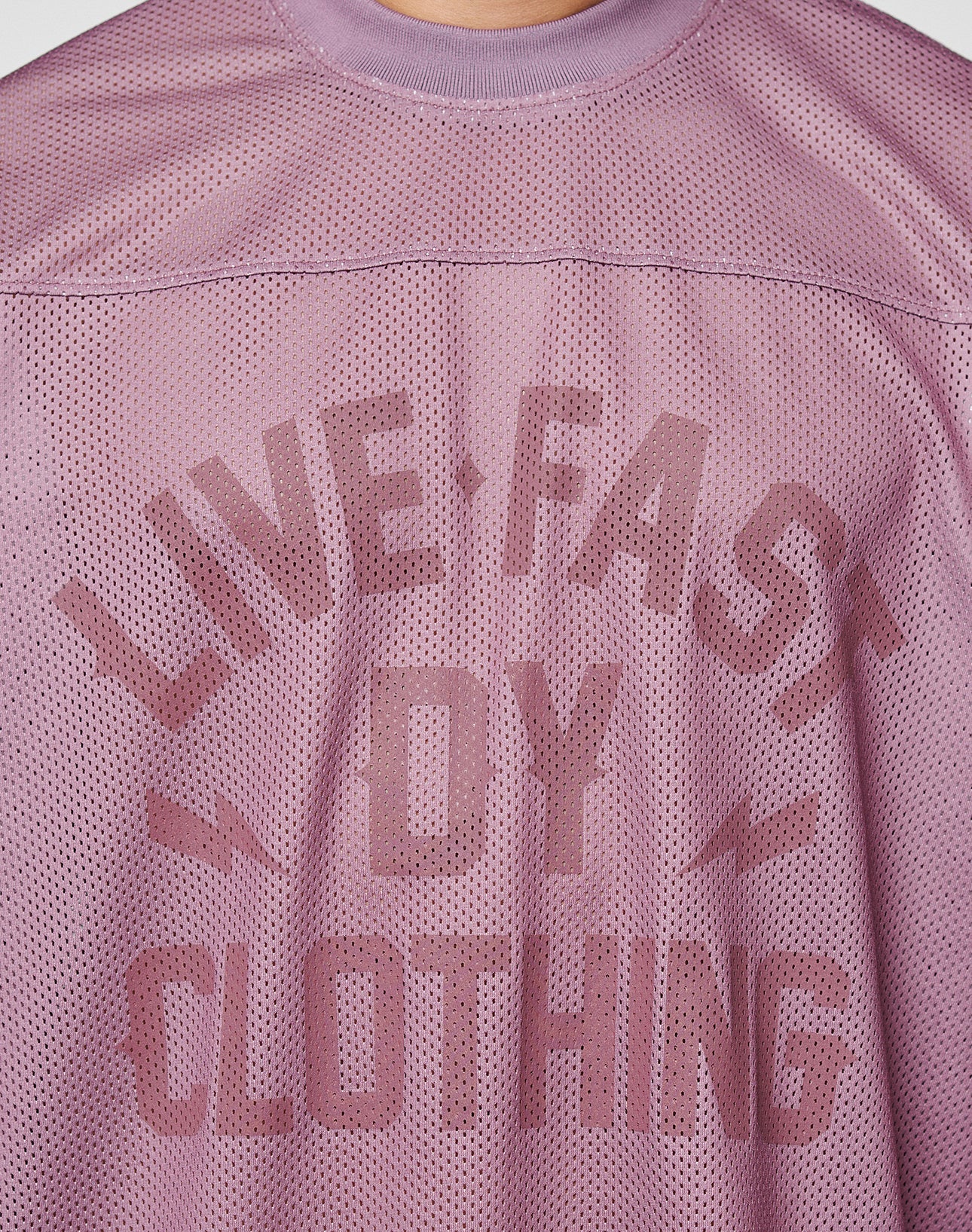 A close-up of the LFDY Flash Jersey by LIVE FAST DIE YOUNG shows its mauve mesh fabric, bold LIVE FAST BY CLOTHING text, lightning bolt graphics, and oversize fit for a modern streetwear vibe.