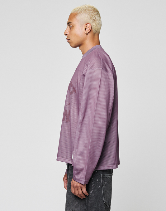 A person with short blond hair stands sideways against a light gray background, wearing the LIVE FAST DIE YOUNG LFDY Flash Jersey—an oversized long-sleeve purple mesh top—and black jeans with white paint splatters.
