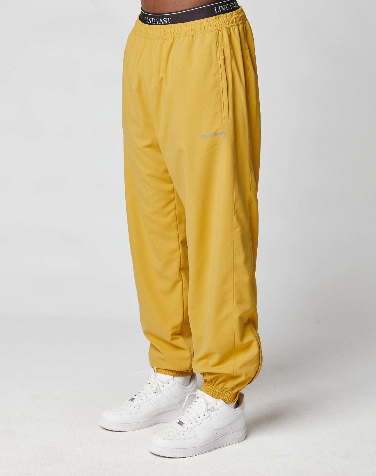 A person wearing LFDY Trackpants by LIVE FAST DIE YOUNG, featuring an elastic waistband with LIVE FAST lettering and elastic cuffs, made from soft polyester, paired with white Nike sneakers against a plain white background.