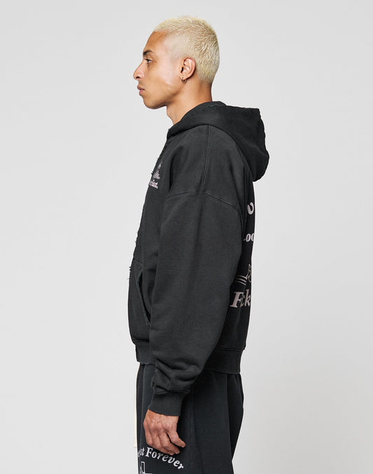 A person with short, bleached blond hair is shown in profile wearing the LIVE FAST DIE YOUNG LFDY Praying Hooded Zip with waffle innenfutter and matching black pants with white text, standing against a plain light gray background.