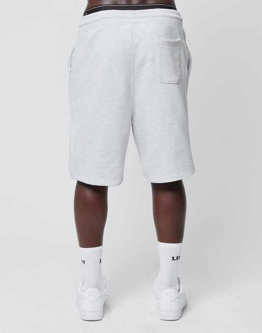 A person faces away, wearing LIVE FAST DIE YOUNG Basic Heavy Shorts in light gray with an elastic waistband and a right-side back pocket, styled with white crew socks and sneakers against a plain white background.
