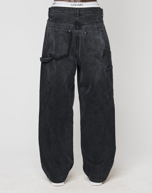 A person wearing LFDY Carpenter Pants by LIVE FAST DIE YOUNG, featuring a loose baggy fit in faded black with large back pockets and a tool pocket, shown from the back against a plain white background.
