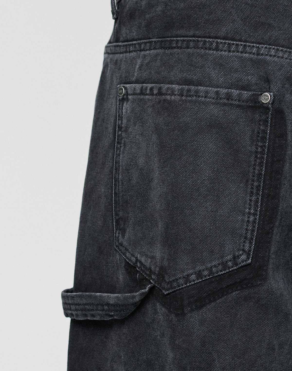 Close-up of the LFDY Carpenter Pants by LIVE FAST DIE YOUNG in black denim, featuring visible stitching and a strap below the pocket for a classic carpenter look against a plain, light gray background.