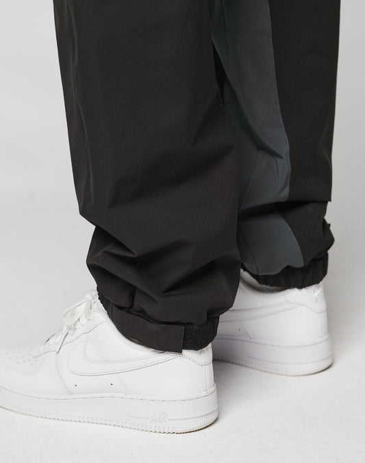 Close-up of a person wearing LIVE FAST DIE YOUNG Basic Shell Pants with elastic waistband, drawstring, and elastic cuffs, paired with white Nike Air Force 1 sneakers. The inside lining of the oversize fit pants is visible.