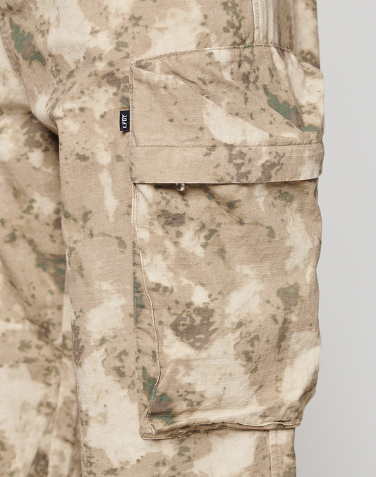 Close-up of the LFDY Cargo pant by LIVE FAST DIE YOUNG in beige and green camo, featuring a wide fit leg, large flap side pocket with Cargo Taschen, and a small black tag on the seam.