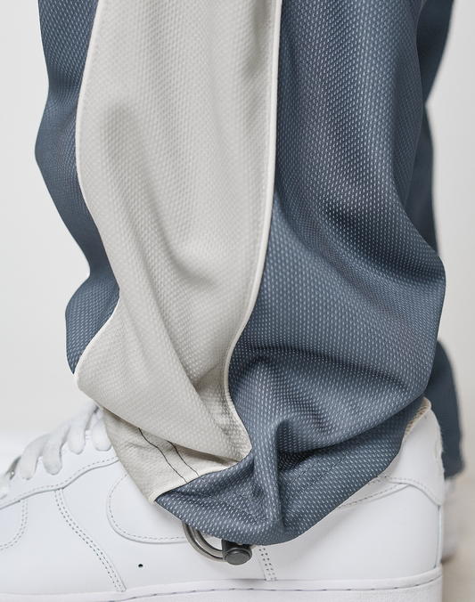 Close-up of a person wearing LIVE FAST DIE YOUNG LFDY DY Trackpants in blue with a light gray stripe, Elastikbund waist, wide fit, and polyester fabric slightly bunching over white sneakers.