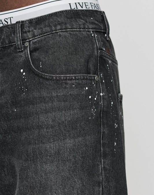 Close-up of a person wearing LFDY Baggy Denim by LIVE FAST DIE YOUNG, featuring individuelle Farbspritzer, with a visible white waistband that reads LIVE FAST in black letters.