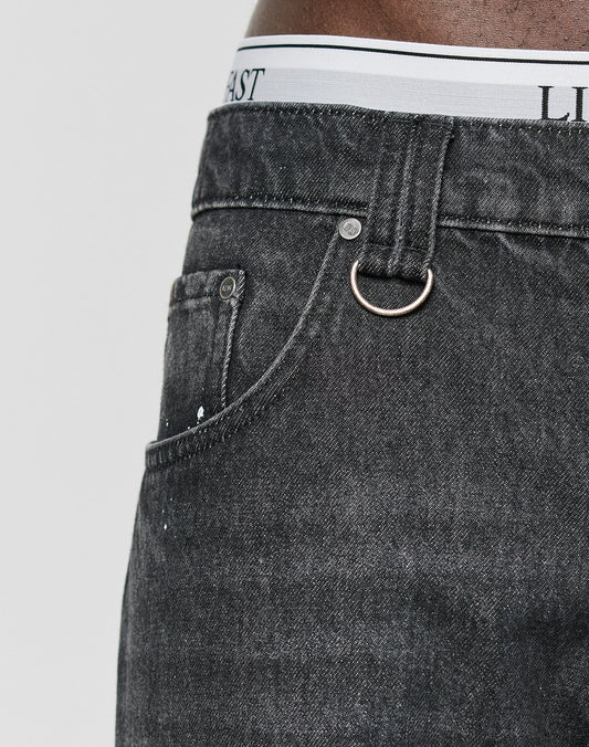 Close-up of a person wearing LFDY Baggy Denim jeans by LIVE FAST DIE YOUNG, featuring a metal ring on the belt loop and white underwear with black text peeking above the waistband, emphasizing the wide straight leg style.