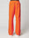 A person is seen from the back wearing LIVE FAST DIE YOUNG’s bright orange Live Fast Trackpants with black piping, a wide elastic waistband, and a reflective logo print, set against a plain light background.