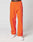 A person wears LIVE FAST DIE YOUNG’s Live Fast Trackpants in bright orange with black details, a Breiter Elastik-Bund, reflektierender Logo Print, and LIVE FAST near the waistband and on one leg, paired with white sneakers.