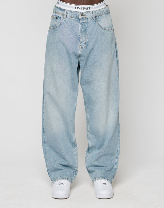 A person wearing light blue LFDY Baggy Denim by LIVE FAST DIE YOUNG, white sneakers, and a visible white waistband with LIVE FAST text, stands against a plain light background.