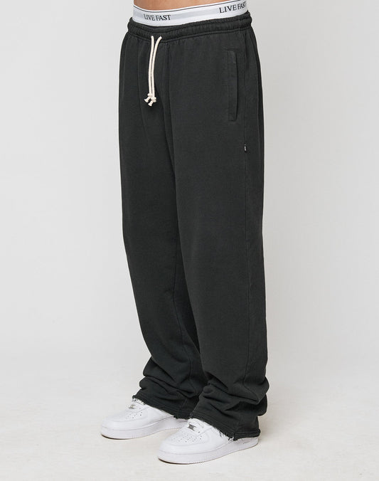 A person in LIVE FAST DIE YOUNG LFDY Lightweight Joggers with elastic waistband and drawstring, paired with white sneakers and a visible white LIVE FAST waistband, stands against a simple light background. | model