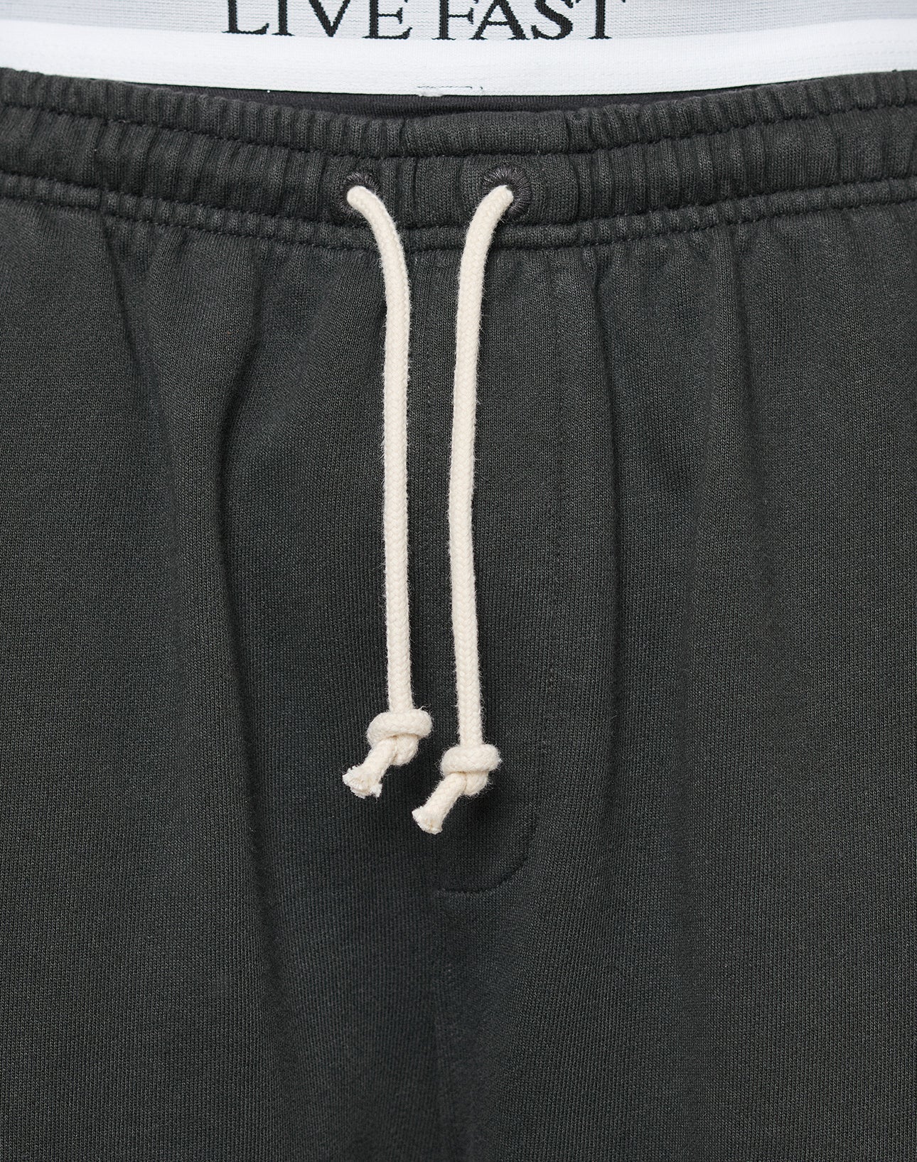 Close-up of the LFDY Lightweight Jogger by LIVE FAST DIE YOUNG—black sweatpants with white knotted drawstrings and LIVE FAST on the inner waistband. Made from soft French Terry fabric for comfort and an oversized fit.