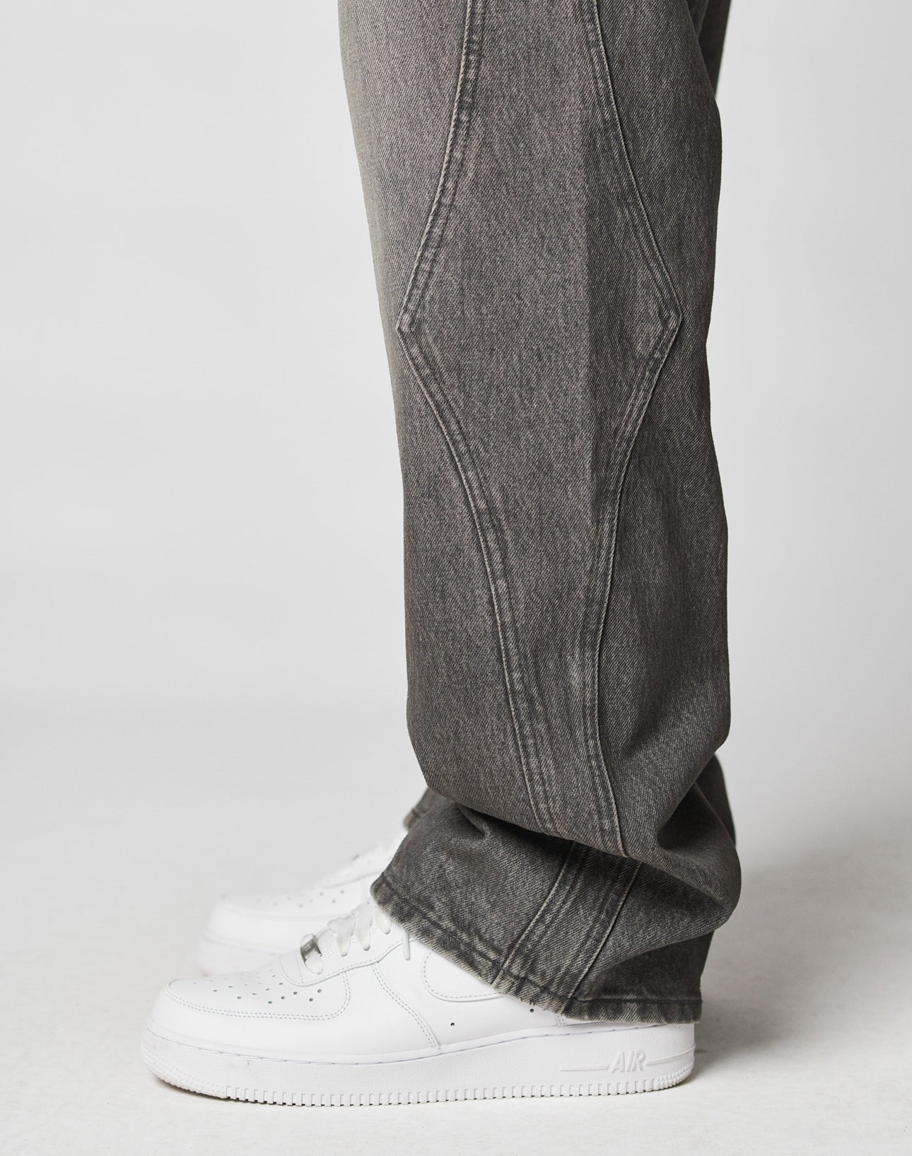 Someone in LIVE FAST DIE YOUNG Rhomb Wide Denim—100% Baumwolle, faded black, baggy fit with a wide straight leg—paired with white Nike Air Force 1 sneakers, stands against a plain white background.