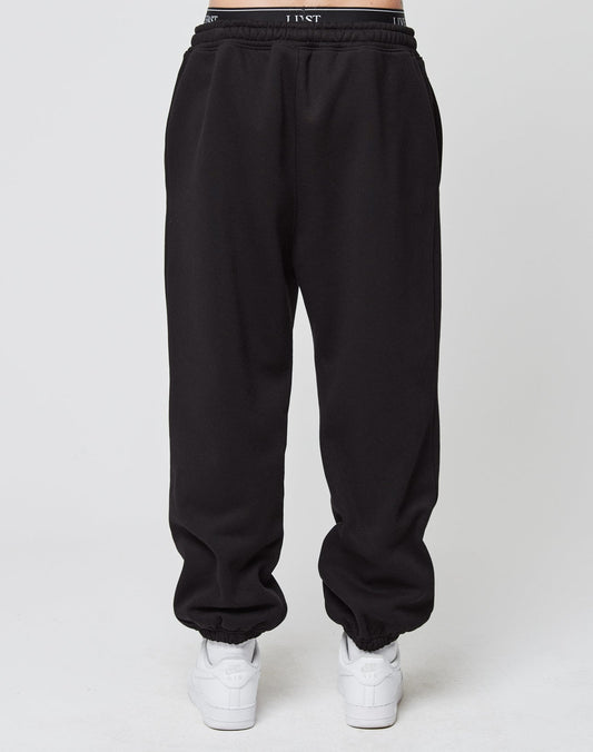 A person wears the LIVE FAST DIE YOUNG Loose Jogger, black sweatpants with elastic cuffs, paired with white sneakers, standing against a plain white background.