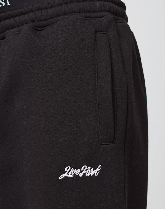 Close-up of the Loose Jogger by LIVE FAST DIE YOUNG: black cotton sweatpants with a vertical pocket and Live Fast embroidered in white near the elastic cuff.