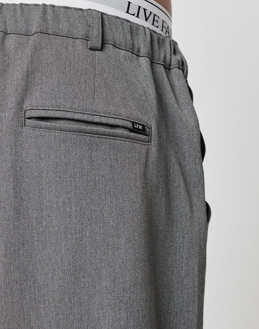 Close-up of the back of gray Wide Casual Pants by LIVE FAST DIE YOUNG with a straight leg and welt pocket. The white underwear’s elastic waistband, featuring LIVE FAST, is visible above the pants.