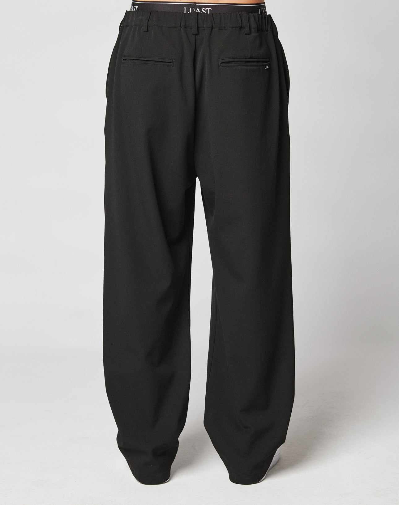 The LIVE FAST DIE YOUNG Wide Casual Pants are loose-fitting black trousers with an elastic waistband, side pockets, two back welt pockets, and subtle text detail. Shown in a modern wide fit style against a plain white background.