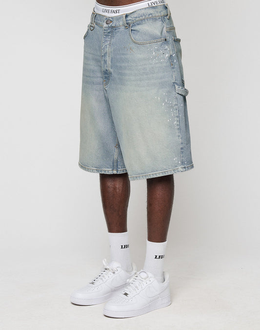A person wears LIVE FAST DIE YOUNG Carpenter Jorts in light blue with Farbspritzer, baggy fit, and 100% Baumwolle, styled with white socks with black text and white Nike Air Force 1 sneakers. Only the lower half is visible.
