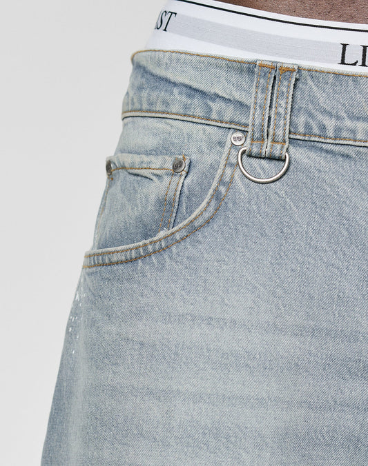 Close-up of a person wearing LIVE FAST DIE YOUNG Carpenter Jorts in a relaxed Baggy Fit with front pocket, belt loops, silver D-ring, and the waistband of white underwear with black text peeking above the jorts.