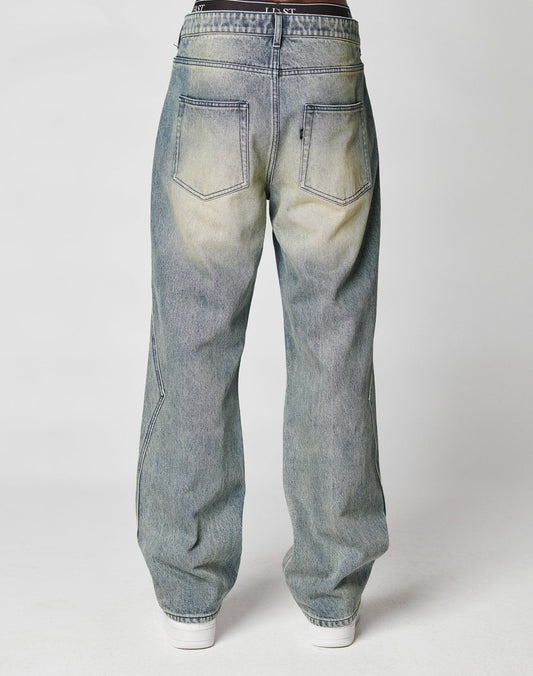 A person is shown from the back against a plain, light background, wearing LIVE FAST DIE YOUNG’s Rhomb Wide Denim in a baggy fit, light blue wash with large back pockets and paired with white shoes.