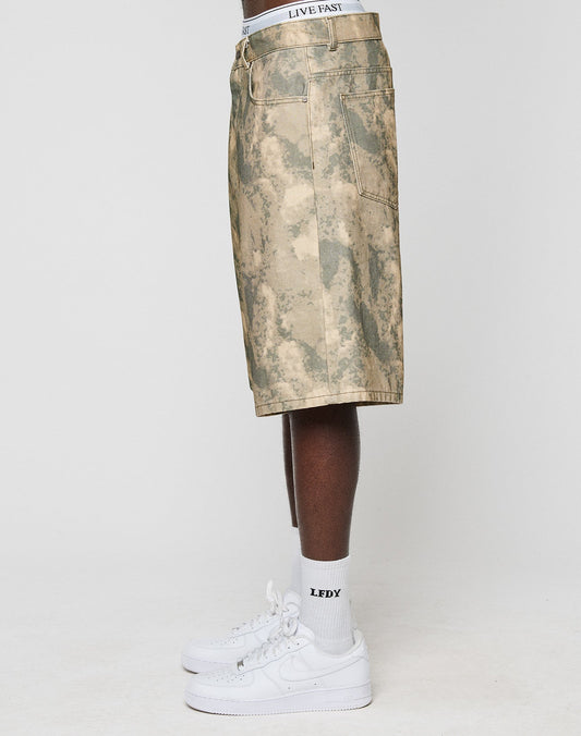 A person stands sideways in beige camouflage Canvas Shorts by LIVE FAST DIE YOUNG, paired with white LFDY waistband boxers, white LFDY socks, and white sneakers against a plain light background.