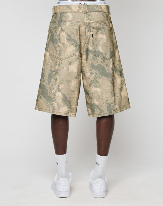 A person faces away, wearing LIVE FAST DIE YOUNG Canvas Shorts (100% Baumwolle, Baggy Fit, gerade Bein) with back pockets. The white waistband of underwear shows above the shorts, paired with white Nike socks and sneakers.