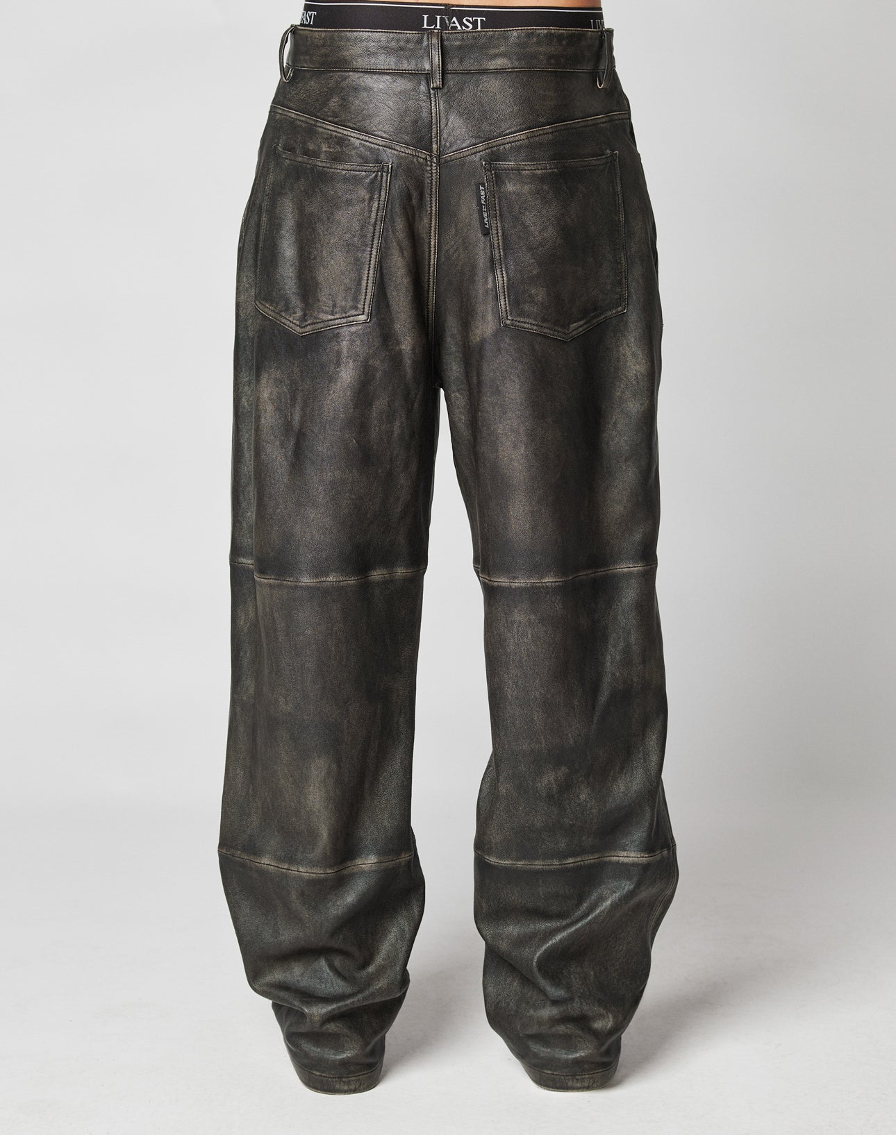 A pair of Baggy Leather Pants by LIVE FAST DIE YOUNG, featuring large back pockets, visible seams, slight fading, and a small flag label, shown from the back against a plain gray background.
