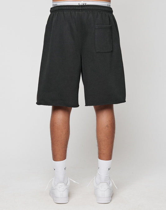 A person stands facing away, wearing black LFDY Praying Shorts by LIVE FAST DIE YOUNG with side pockets and a back pocket, paired with white crew socks and sneakers against a plain light background.