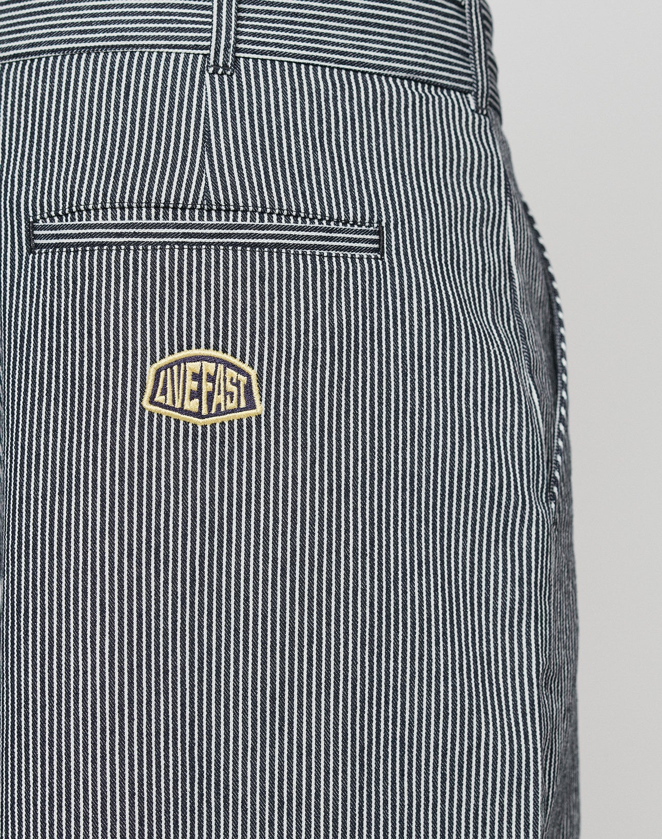 Close-up of LFDY Twill Shorts by LIVE FAST DIE YOUNG, featuring black and white stripes, a back pocket with a yellow LIVE FAST patch, visible waistband and side seam, oversize fit, and wide straight leg for a relaxed style.