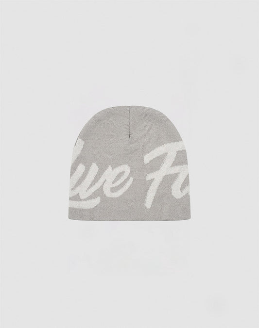 The LFDY Jacquard Beanie by LIVE FAST DIE YOUNG is a light gray knit beanie made from 100% Polyacryl, with large white cursive text partially visible across the front, shown against a plain white background.