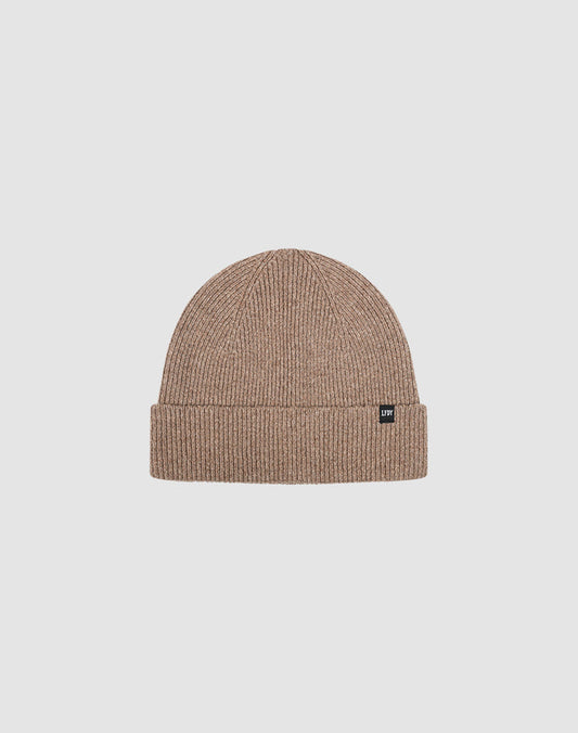 The Live Fast Boucle Beanie by LIVE FAST DIE YOUNG is a light brown ribbed polyester beanie with a folded brim and a small black flag-label on the front, shown against a plain light gray background.| plain 