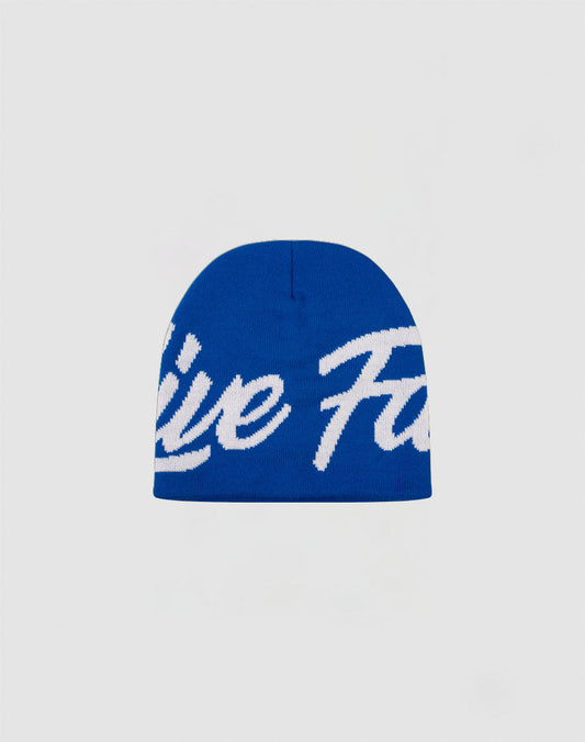 The LFDY Jacquard Beanie by LIVE FAST DIE YOUNG is a blue Polyacryl hat with large white cursive text across the front, shown on a plain light gray background.