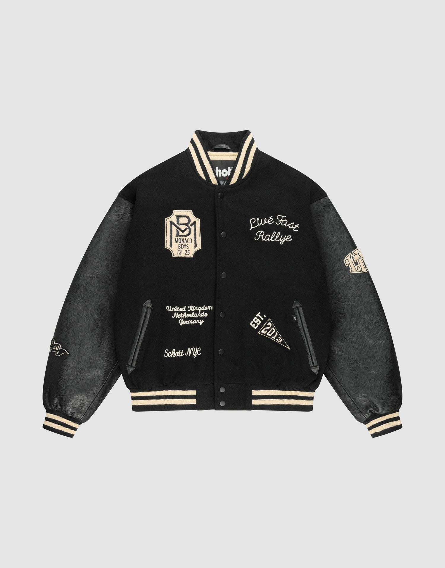 A person stands against a light background wearing cream pants and the LFDY x Schott NYC Varsity Jacket by LIVE FAST DIE YOUNG, featuring beige LIVE FAST and LÉQUIPE CÔTE DAZUR lettering on the black back.