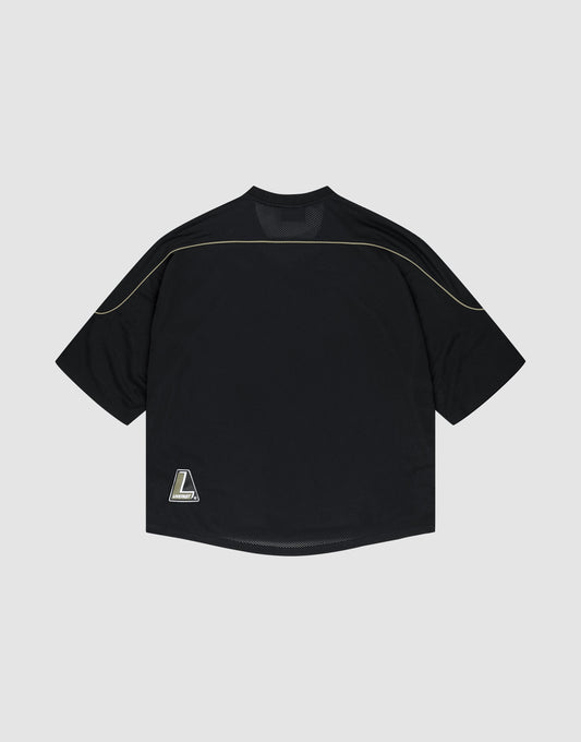 The LIVE FAST DIE YOUNG Basic Mesh Jersey is a black, oversized short-sleeve shirt with gold piping on the shoulders and a small L logo patch at the bottom left hem, made from polyester and shown against a light gray background.