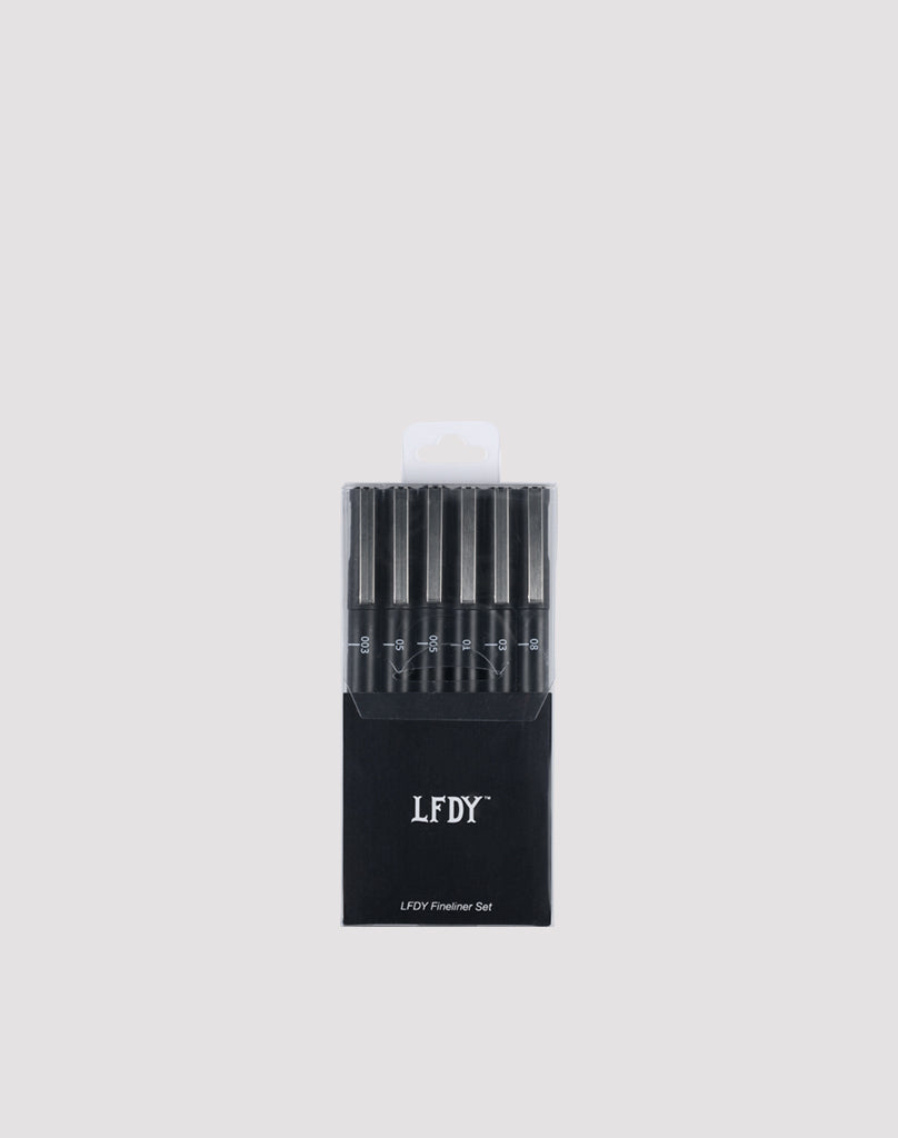 A black box labeled LIVE FAST DIE YOUNG LFDY Fineliner Set holds six wasserfest black fineliner pens with varying line widths, arranged vertically cap-up against a plain light gray background.| plain 