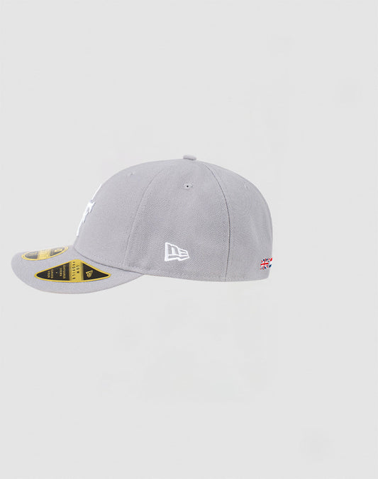 The LFDY x NEW ERA 59FIFTY Low Profile Cap by LIVE FAST DIE YOUNG is shown in light grey, with the New Era logo on the left, a small Union Jack near the back, and stickers still on its flat brim.
