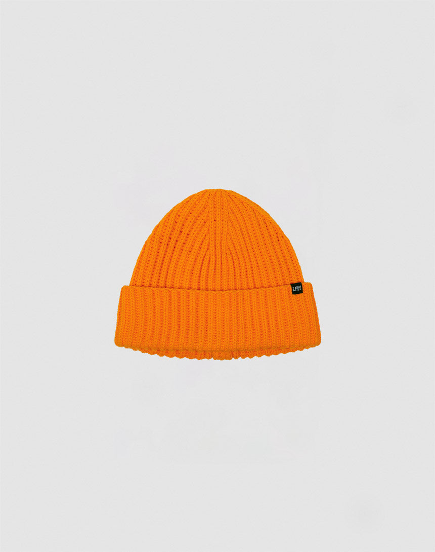 The LIVE FAST DIE YOUNG Rib Knit Beanie in bright orange features a folded brim and a small black side tag, shown against a plain light gray background.