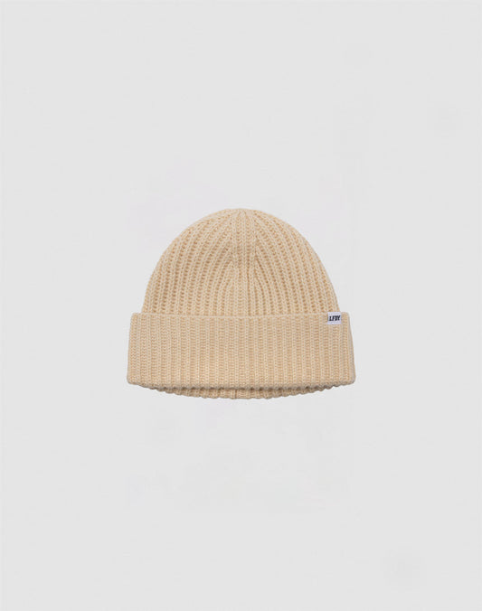 Die Rib Knit Beanie von LFDY in Beige besteht aus 100% Acryl, hat einen gefalteten Bund und ein kleines weißes Rechteck-Label an der Seite – präsentiert vor einem schlichten hellgrauen Hintergrund.