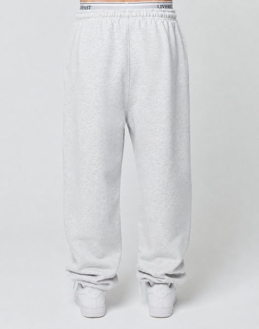 A person wears LIVE FAST DIE YOUNG Basic Loose Jogger sweatpants in light gray with an elastic waistband and loose fit, paired with white sneakers, standing against a plain white background. The joggers look comfortable and relaxed.